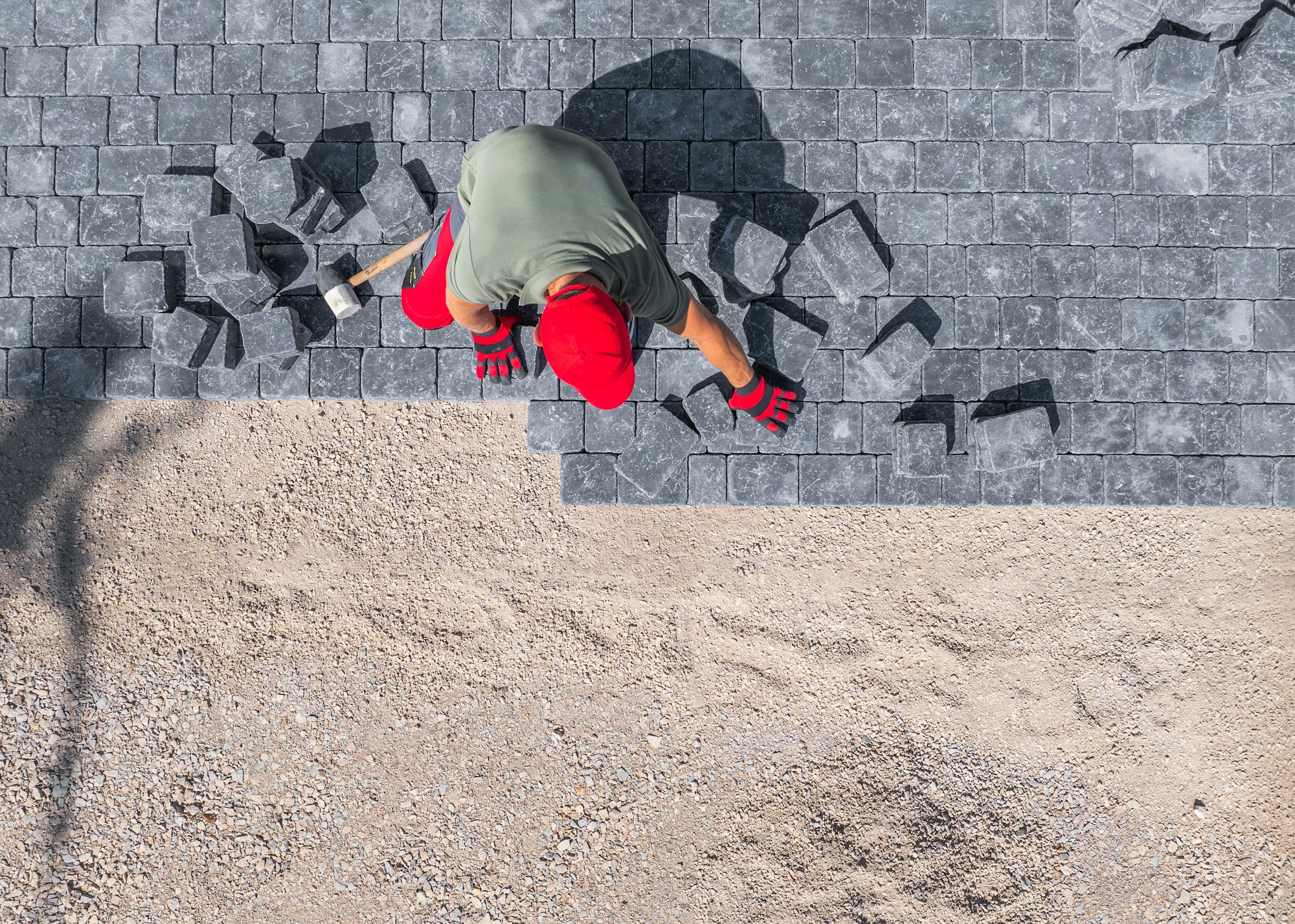 A Worker Laying Paver Stones on a Driveway Under the Midday Sun in a Residential Area