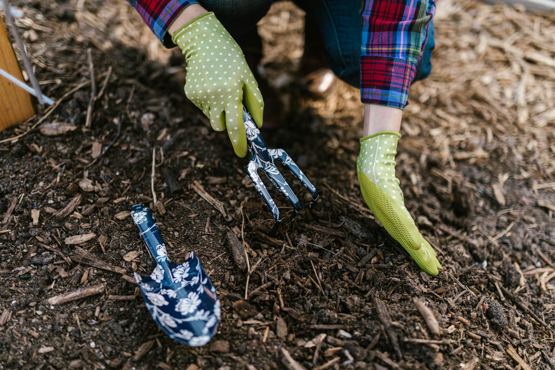 person wearing green gloves holding garden tools